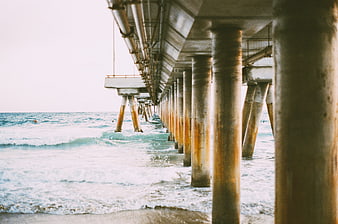 Underneath a pier with ocean waves and concrete pillars