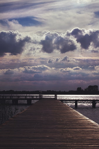 Dramatic wooden pier extending into lake under cloudy sky