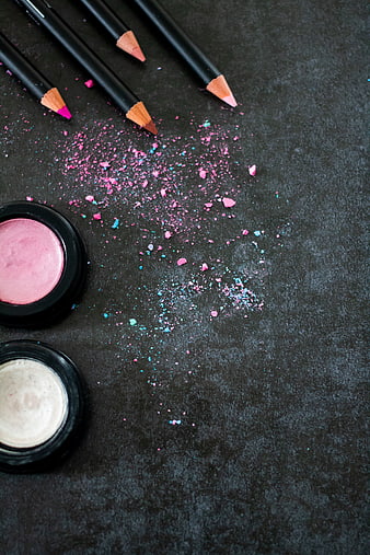 Cosmetic pencils and eyeshadow on dark textured background