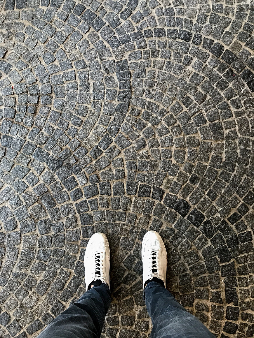 First-person view of white sneakers on cobblestone street