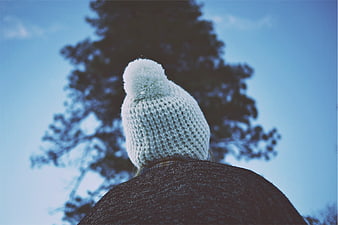 Person wearing white knit beanie with pom pom outdoors