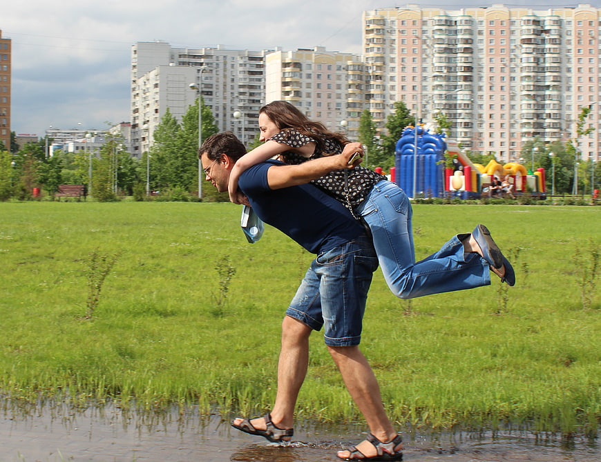 Man Carrying Woman Through Puddle In Urban Park