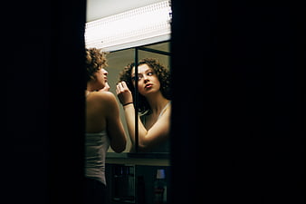 Young woman looking in bathroom mirror with dark frame