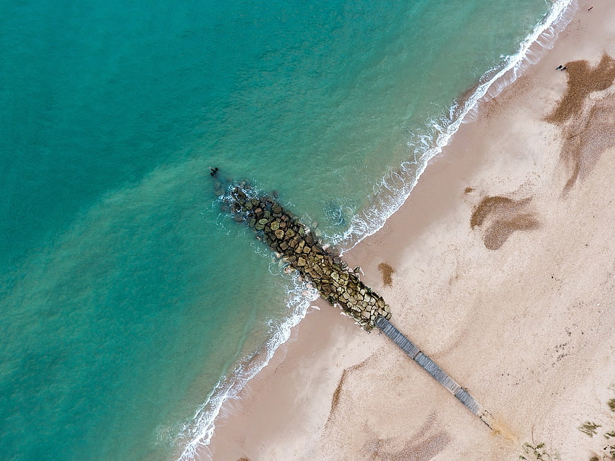 Aerial View of Turquoise Ocean and Sandy Beach with Jetty
