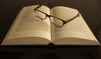 Open book with reading glasses on dark table