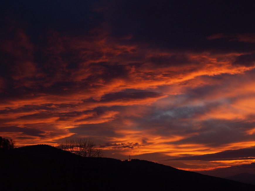 Dramatic fiery orange sunset sky over dark mountain silhouette