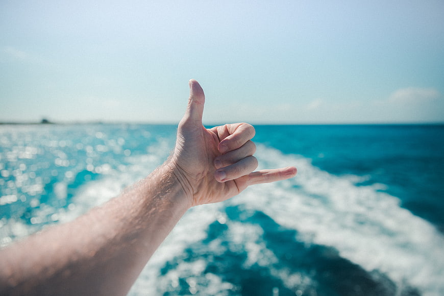 Man's hand making shaka sign over turquoise ocean waves