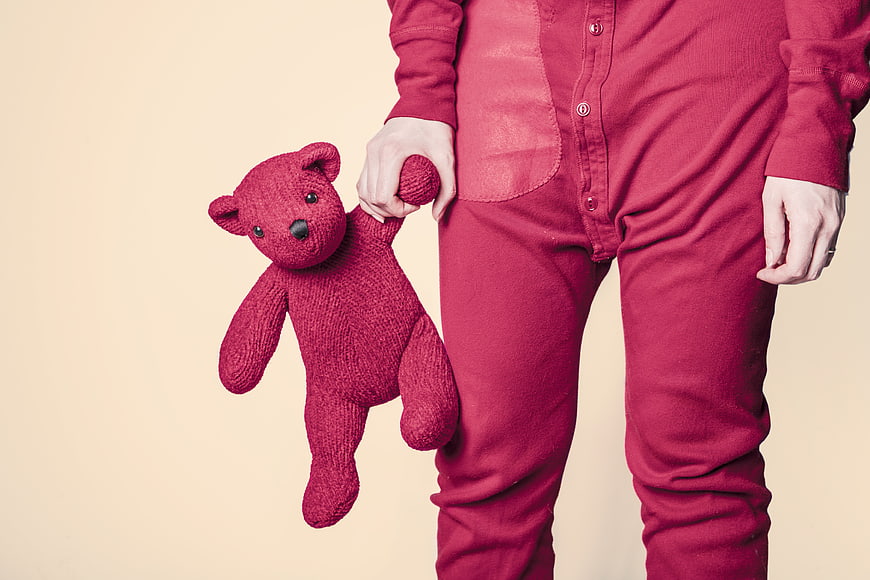 Child in red onesie holding matching knitted teddy bear
