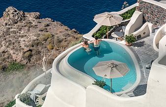 Couple relaxing in infinity pool overlooking Santorini sea