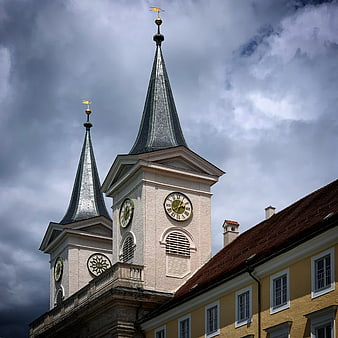 Baroque church towers with clock against dramatic cloudy sky