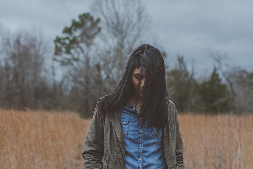 Melancholic woman with long dark hair standing in a field