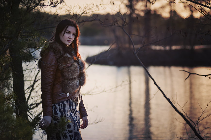 Woman in Leather Jacket and Fur Scarf by Lake at Sunset