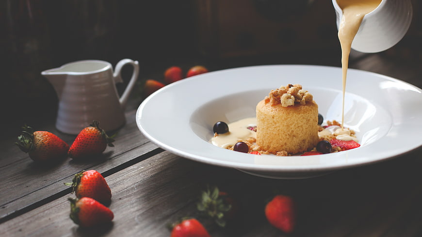Pouring caramel sauce on a mini sponge cake with strawberries