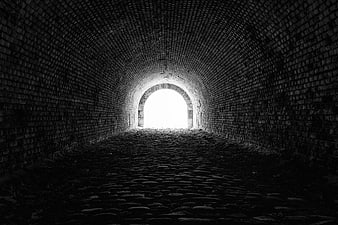 Black and white view of a brick tunnel leading to a bright exit