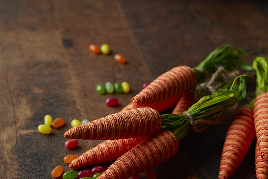Handmade yarn carrots with jelly beans on rustic wood