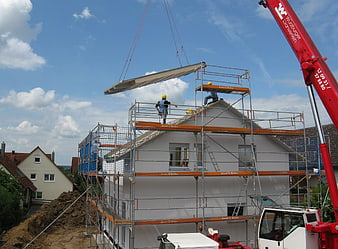Construction workers installing roof beam with crane