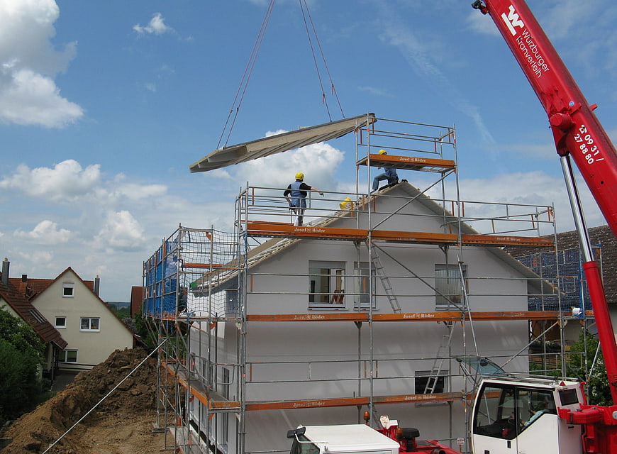 Construction workers installing roof beam with crane