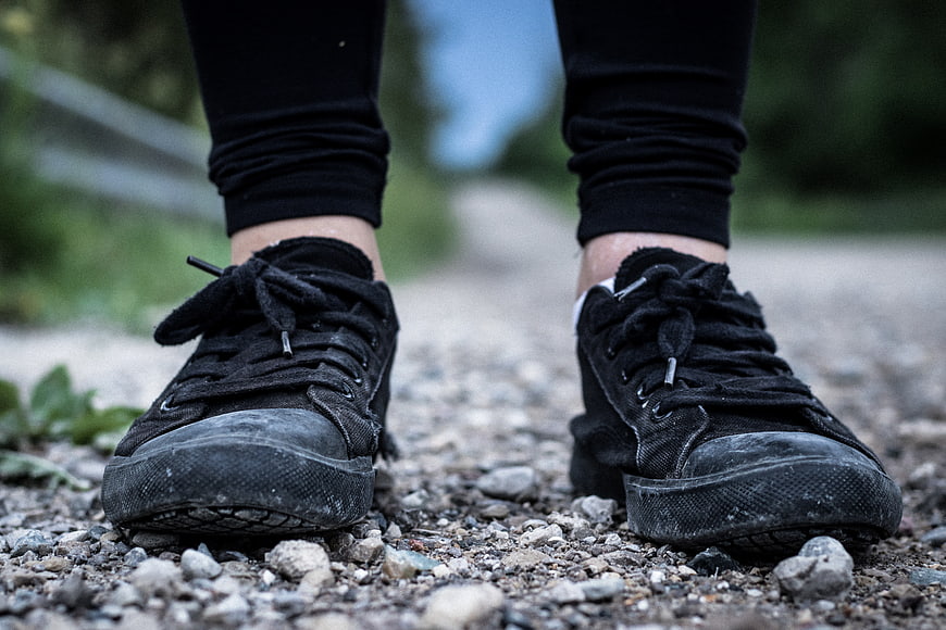 Close-up of worn black sneakers on gravel path