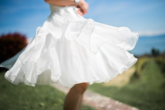 Woman in white dress twirling outdoors on sunny day