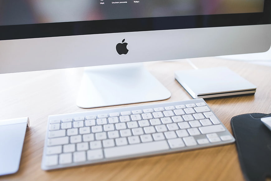 Close-up of Apple iMac, keyboard, and accessories on wooden desk
