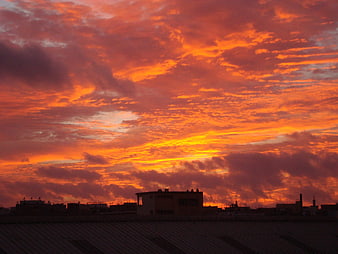 Dramatic orange sunset sky over city rooftops and silhouette