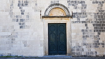 Old Stone Wall with Arched Doorway and Dark Wooden Doors