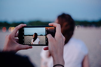 Hands holding smartphone taking photo of woman on beach at dusk