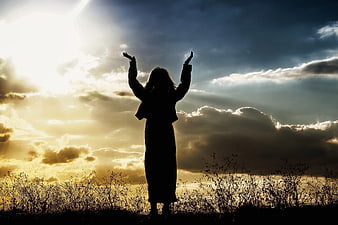 Silhouette of woman with raised arms praying at sunset
