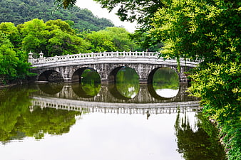 Traditional Stone Arch Bridge Over Calm River With Lush Green Reflections