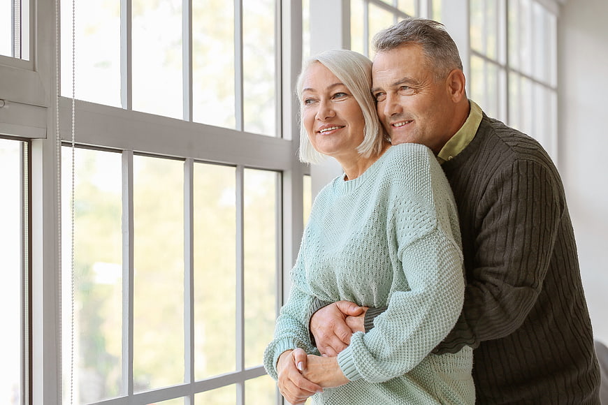 Happy Senior Couple Embracing by Window