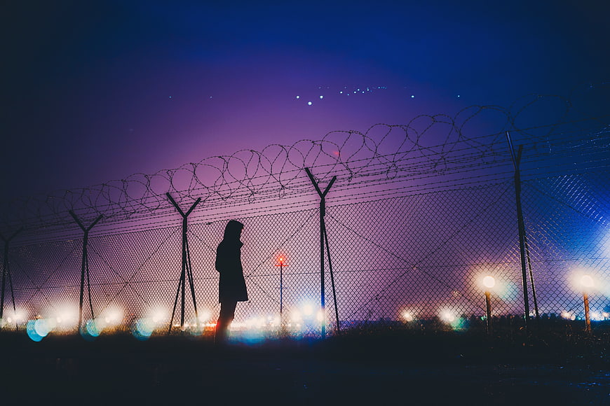 Silhouette of person standing by barbed wire fence at night