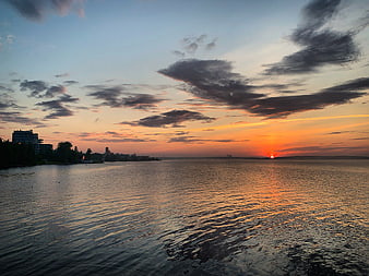 Vibrant Sunset Over Calm Water with City Skyline Silhouette
