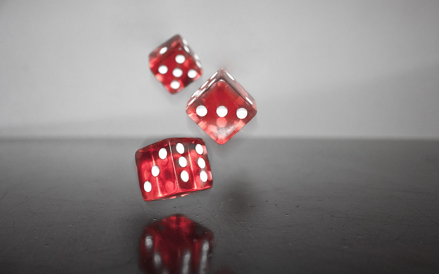 Three red dice falling on a dark reflective surface