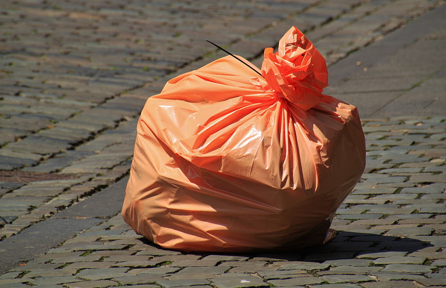 Orange plastic trash bag on cobblestone street
