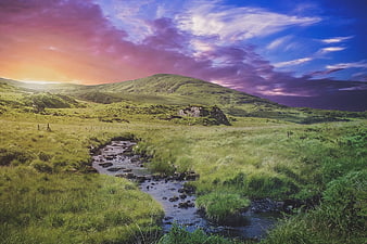 Dramatic sunset landscape with stream and rolling green hills