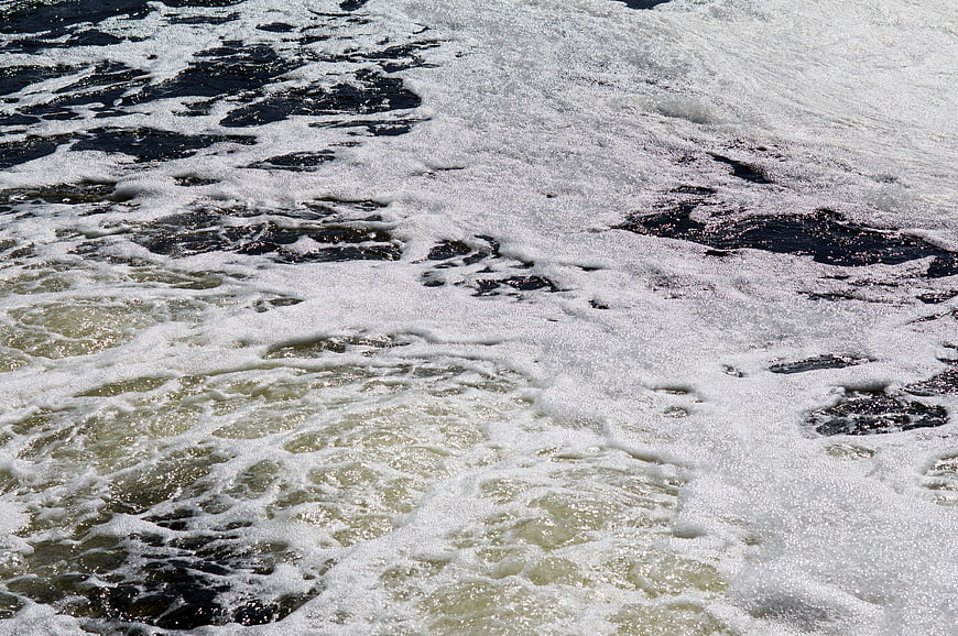 Polluted River Water Surface With Dark Sewage Foam And Bubbles