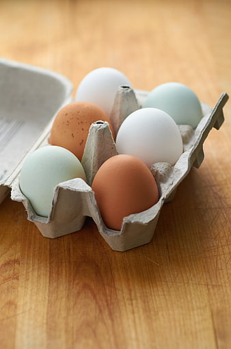 Colorful eggs in a carton on a wooden table