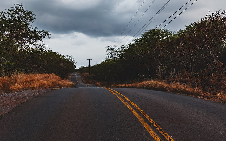 Empty asphalt road with yellow lines under cloudy sky