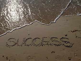 Success written in wet sand at the shoreline with ocean waves