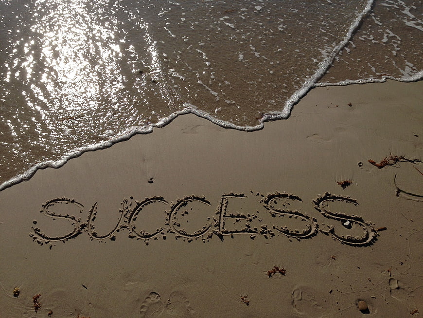 Success written in wet sand at the shoreline with ocean waves