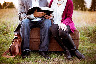Couple reading a book together on an armchair in a grassy field