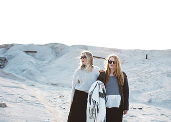Two women walking on white sand dunes in winter fashion