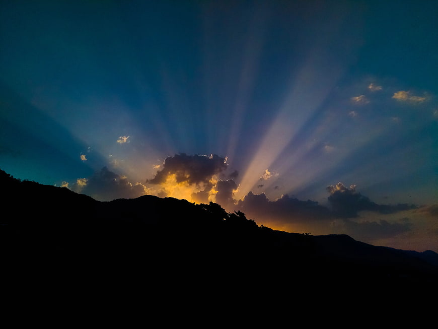 Dramatic sun rays bursting over mountain silhouette at sunset