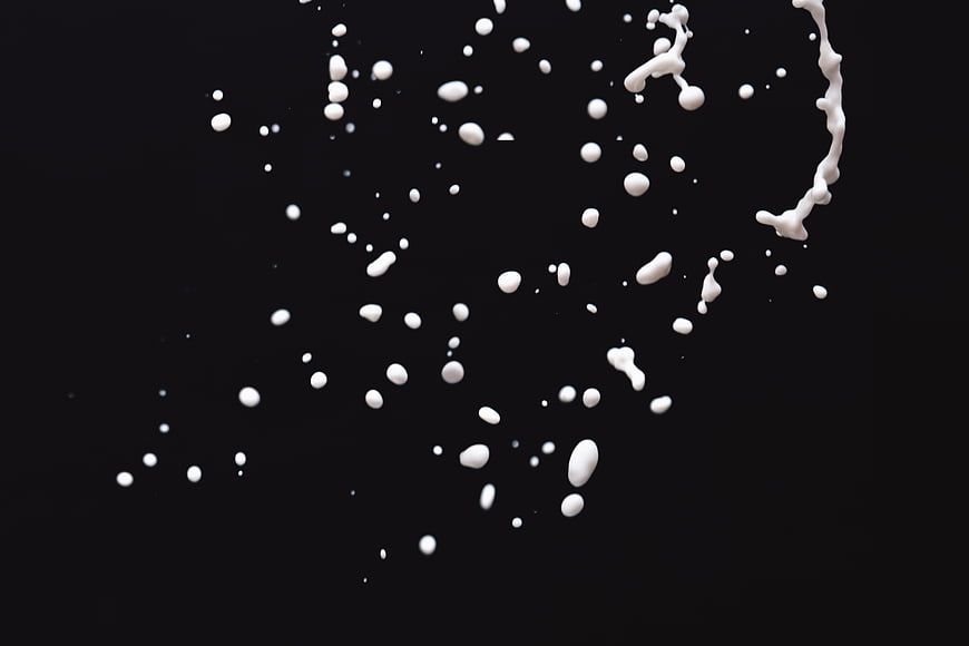 White liquid milk splash droplets on black background