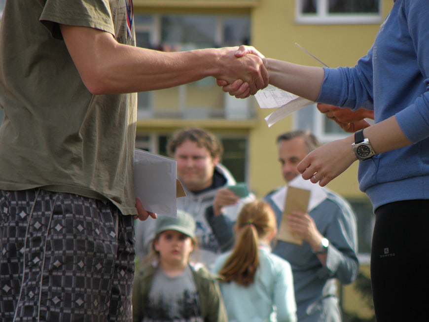 Close-up of two people shaking hands outdoors with a group in the background