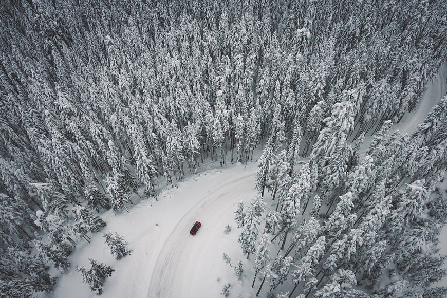 Aerial View of Red Car Driving on Snowy Forest Road