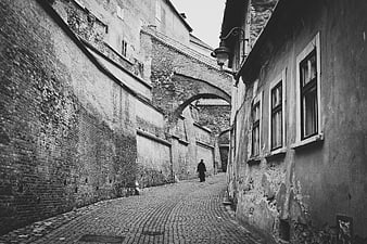 Black and white photo of a man walking down a narrow cobblestone alley