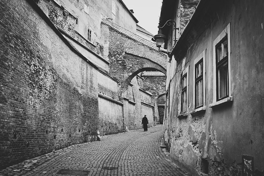 Black and white photo of a man walking down a narrow cobblestone alley
