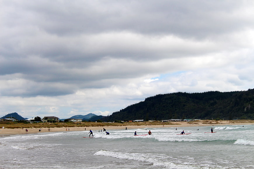Surfers on Beach Under Cloudy Sky with Forested Hills