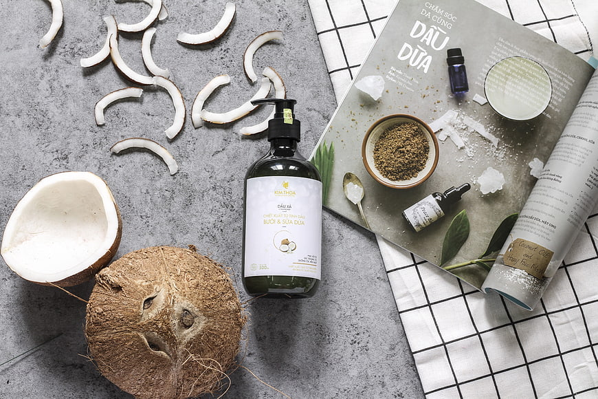 Flat lay of coconut shampoo bottle with fresh coconuts and magazine